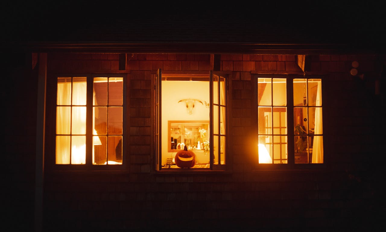 Warm glowing pumpkin seen through a home window, setting a cozy Halloween atmosphere.