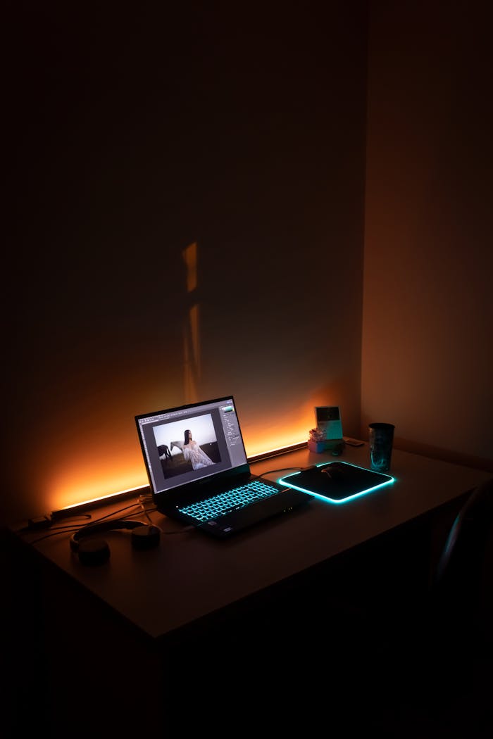 A dimly lit workspace featuring a glowing laptop and mouse pad in İzmir, Turkey.