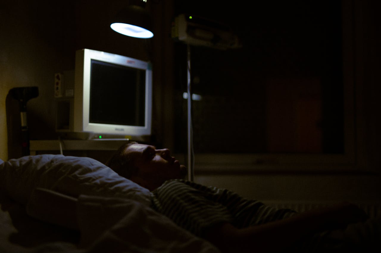 menu-02 Man lying on a hospital bed under dim light, with medical equipment visible.