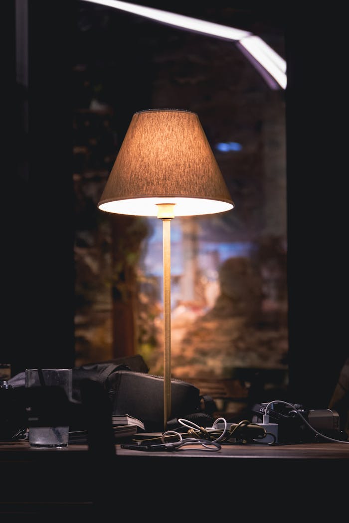 Warm desk lamp casting soft light on a cluttered workspace with a dark, cozy ambiance.