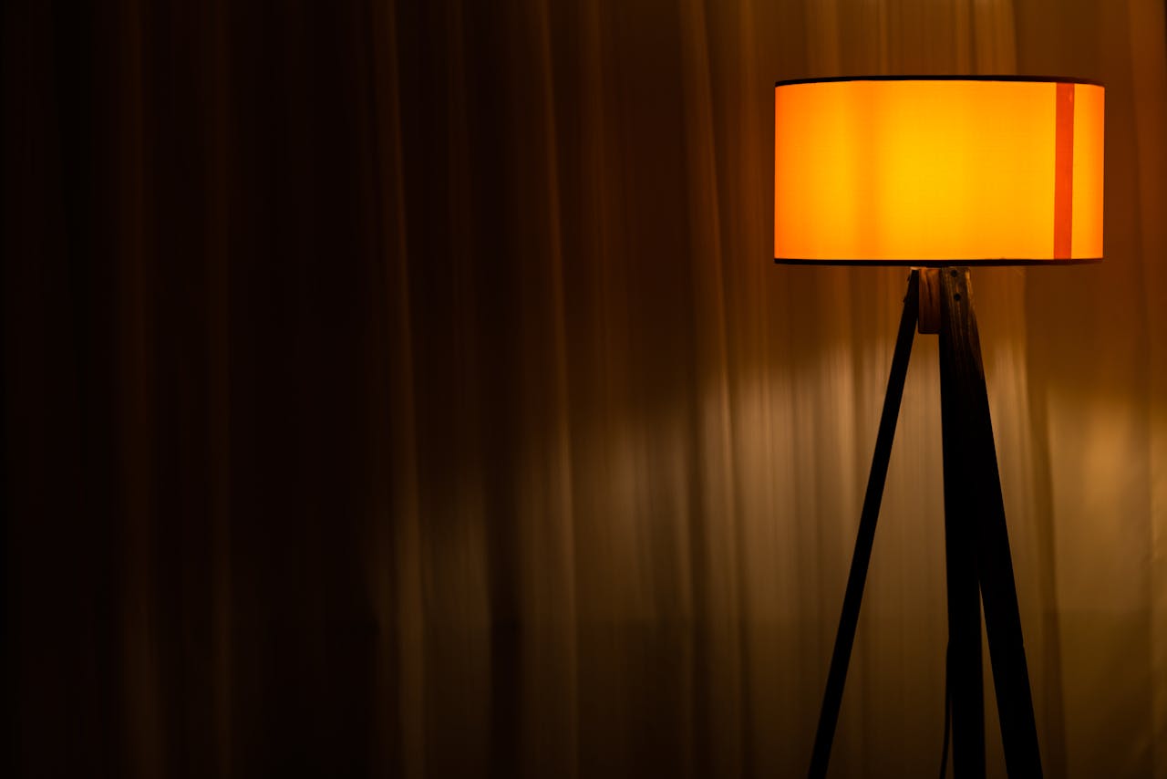 Elegant orange floor lamp casting a warm glow in a minimalist, dark room. Perfect for cozy interior decor.